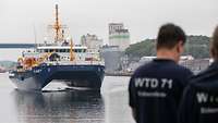 Two people are waiting for the vessel that is about to enter the port