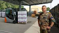 Ein Soldat steht vor Containern unter einem Schleppdach, im Hintergrund ist ein Gabelstapler bei der Arbeit.