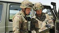 Zwei Soldaten stehen vor einem Fahrzeug und lesen einen Prüfbericht
