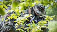 Zwei Soldaten knien mit Waffe in der Hand im Wald.