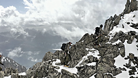 Auf einem Felsweg laufen drei Soldaten in großer Höhe die letzten Meter zu einem Berggipfel, im Hintergrund eine Bergkette.