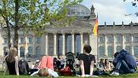 Junge Erwachsene und Kinder beim Chillen auf der Wiese vor dem Reichstagsgebäude in Berlin