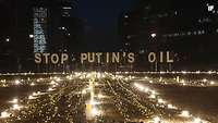 Abendlicher Protest mit dem Schriftzug Stop Putin´s Oil. Tausende brennende Kerzen bilden das Zeichen des Friedens