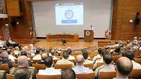 Exercise Director Colonel Kraus standing on the lecture theatre stage while participants are listening to his briefing. 