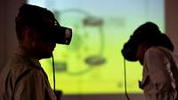 The silhouettes of two soldiers with VR goggles in front of a bright presentation screen.