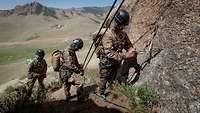 Drei mongolische Soldaten bereiten an einem Fels ihre Sicherheitsseile für den Aufstieg vor.