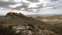 Steppenartige, karge Landschaft mit schroffer Felsformation und dramatischen Wolken am Himmel