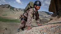 Ein mongolischer Soldat klettert auf felsigem Untergrund den Berg hinauf, im Hintergrund Berge.