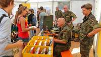 Soldaten und Besucher in einem Zelt. Gelbe Postkisten mit Briefen stehen auf den Tischen.