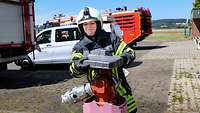 Eine junge Feuerwehrfrau in Uniform und Schutzhelm dreht auf einem Flugplatz einen Wasser-Hydranten auf