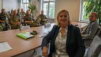 Eine Frau lächelt in die Kamera, dahinter sitzen Soldaten.