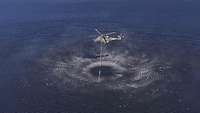 Ein Hubschrauber schwebt über einem See und taucht den angehängten Löschwasserbehälter in das Wasser