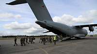 Mehrere Soldatinnen und Soldaten steigen durch die geöffnete Heckklappe eines militärischen Flugzeuges aus.