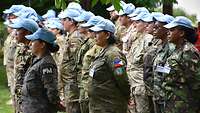 Soldatinnen und Soldaten verschiedener Nationen sind in Formation auf einer Wiese angetreten. 