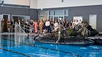 In einem Schwimmbecken sitzen Soldaten mit Hund in einem Schlauchboot.