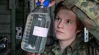 Die Soldatin hält ein großes Glas mit Dieselkraftstoff in ihren Händen 