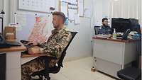 Ein deutscher und ein bangladeschischer Soldat sitzen in einem Büro und arbeiten an Computern