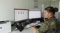 Eine Soldatin sitzt in einem Arbeitscontainer vor zwei Bildschirmen und telefoniert