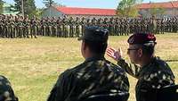 Zwei Soldaten im Gespräch, im Hintergrund stehen mehrere angetretene Soldatinnen und Soldaten