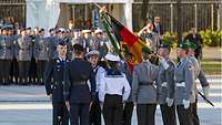 Neun Soldaten in Dienstanzügen stehen in Grundstellung sich gegenüber, einer von ihnen hält die Deutschlandflagge