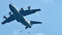 Ein Flugzeug vom Typ A400M fliegt unter blauem Himmel, zwei Soldaten sind abgesprungen.