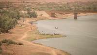 Aus der Vogelperspektive ist der Niger zu sehen, der durch eine Brücke fließt, am Ufer und im Wasser sind Einwohner erkennbar
