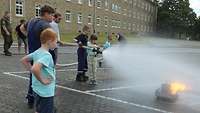Kinder versuchen unter Anleitung der Feuerwehr ein Feuer zu löschen.