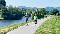 Zwei Männer laufen in Sportkleidung an einem Fluss entlang