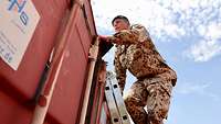 Ein Soldat mit schwarzem Barett klettert über eine Leiter auf das Dach eines Seecontainers