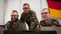 Die drei im Text genannten Soldaten blicken während der CWIX von ihren Computern in die Kamera. 