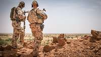 Zwei Soldaten stehen auf einer felsigen Erhöhung und schauen über Wüstengebiet.