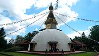 Ein weißer nepalesischer Tempel, an seiner Spitze sind nach allen Richtungen Fähnchen ausgerichtet. 