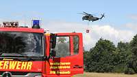 Ein Feuerwehrwagen mit offener Fahrertür und ein Hubschrauber der Bundeswehr im Einsatz