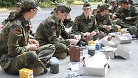Jugendliche sitzen auf dem Boden, vor ihnen liegt der Inhalt von Einmannpackungen der Bundeswehr.