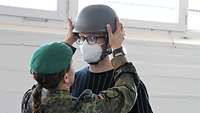 Eine Soldatin setzt einem jungen Mann einen Militärhelm auf.