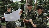 Zwei Männer und eine Frau stehen in Uniform im Wald und orientieren sich mit einer Karte.