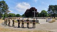 Die Soldaten stellen sich um das Betonkreuz des Friedhofs herum auf.