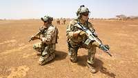 Mehrere Soldaten knien mit ihren Gewehren im roten Wüstensand Afrikas.