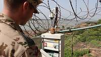 Ein Soldat kontrolliert den Stromkasten einer Überwachungskamera, die von Stacheldraht umgeben ist