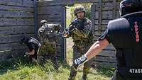 In einem Holzhaus treffen Soldaten mit Helm und Gewehrattrappen auf gepolsterte Gegner in einer Kampfübung