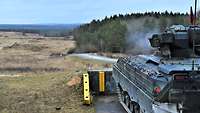 Blick auf die Schießbahn, rechts ein Schützenpanzer, dessen Bordmaschinenkanone gerade feuert.