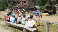 Vorführung von Indianer-Darstellern in einer Westernstadt, davor sitzen Kinder auf einer Holzbank.