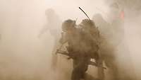 Soldaten mit Rucksäcken und Gewehren stürmen durch eine Staubwolke