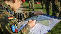 Eine Soldatin blickt auf ein Klemmbrett mit einer Karte und einer Skizze. 