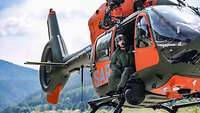 Ein Soldat sitzt in der geöffneten, orangefarbenen Seitentür eines Hubschraubers, der schwebt.