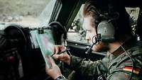 Ein Soldat sitzt mit Kopfhörern in seinem Fahrzeug und überträgt Koordinaten in eine Lagekarte