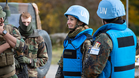 Zwei Soldatinnen, beide tragen blaue Schutzwesten und einen blauen UN-Helmüberzug, im Gespräch mit zwei Soldaten.