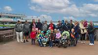 Eine Menschengruppe mit Kindern steht für ein Gruppenfoto am Meer.