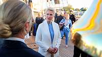 Eine Frau, mit blonden Haaren in einem weißen Anzug, spricht mit einem Marinesoldaten.