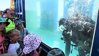 Ein Marinetaucher zeigt seine Arbeit Unterwasser mehreren Kindern.
